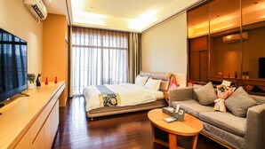 Habitación de hotel con cama, sofá, televisión, escritorio y una ventana grande con cortinas.