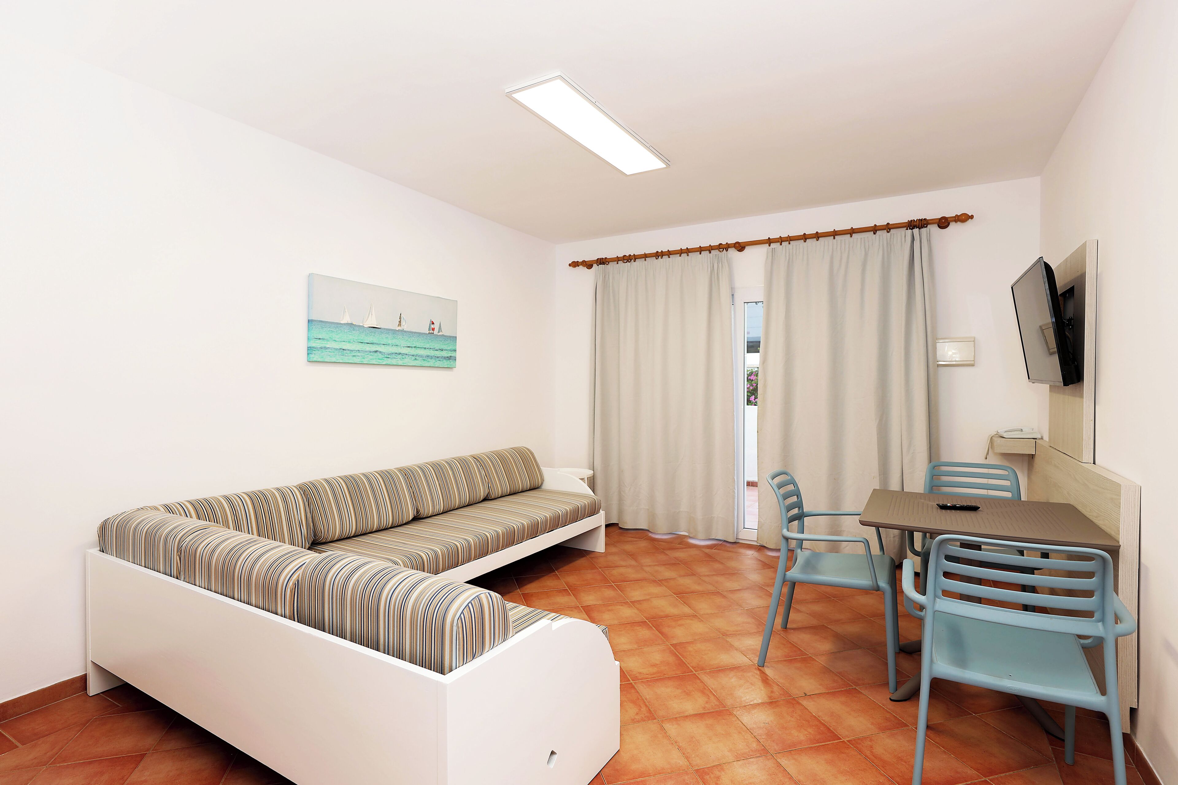 Una habitación con sofá, una mesa de comedor con sillas, un televisor y un cuadro en la pared.