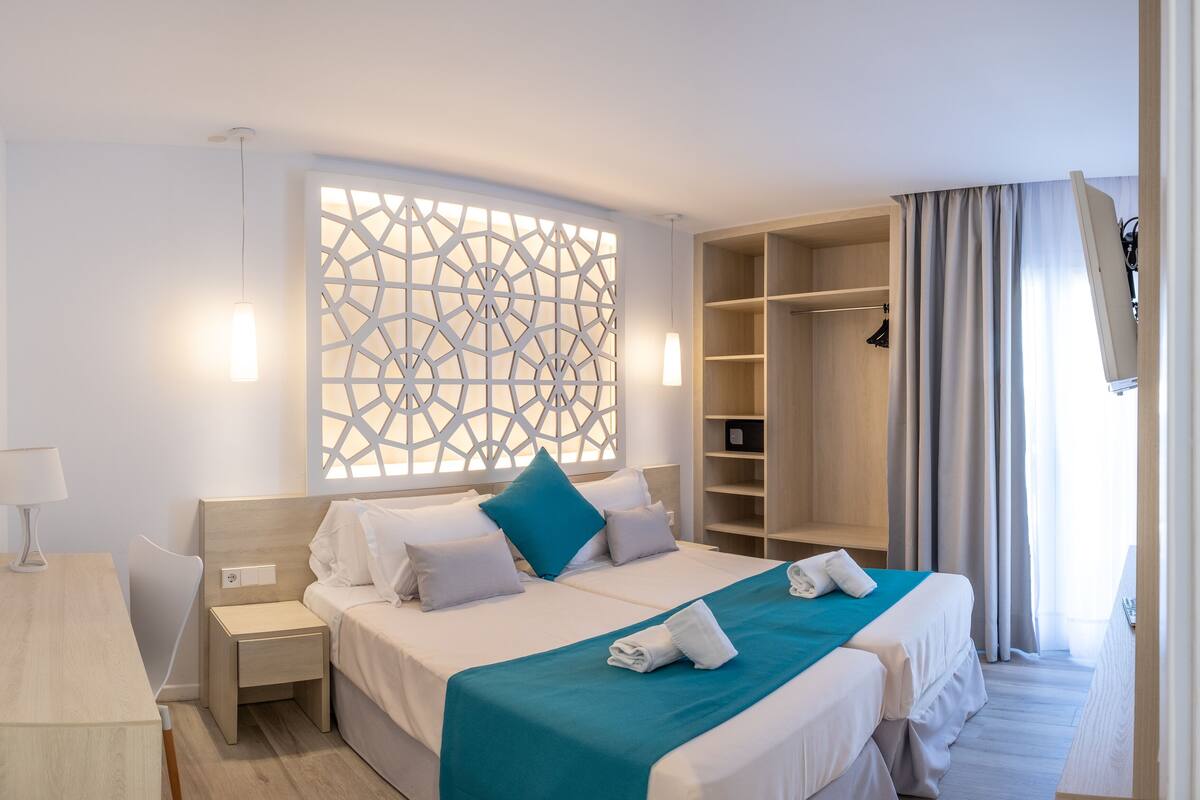 A hotel room with a large bed, a nightstand, a wardrobe, and a decorative wall panel.