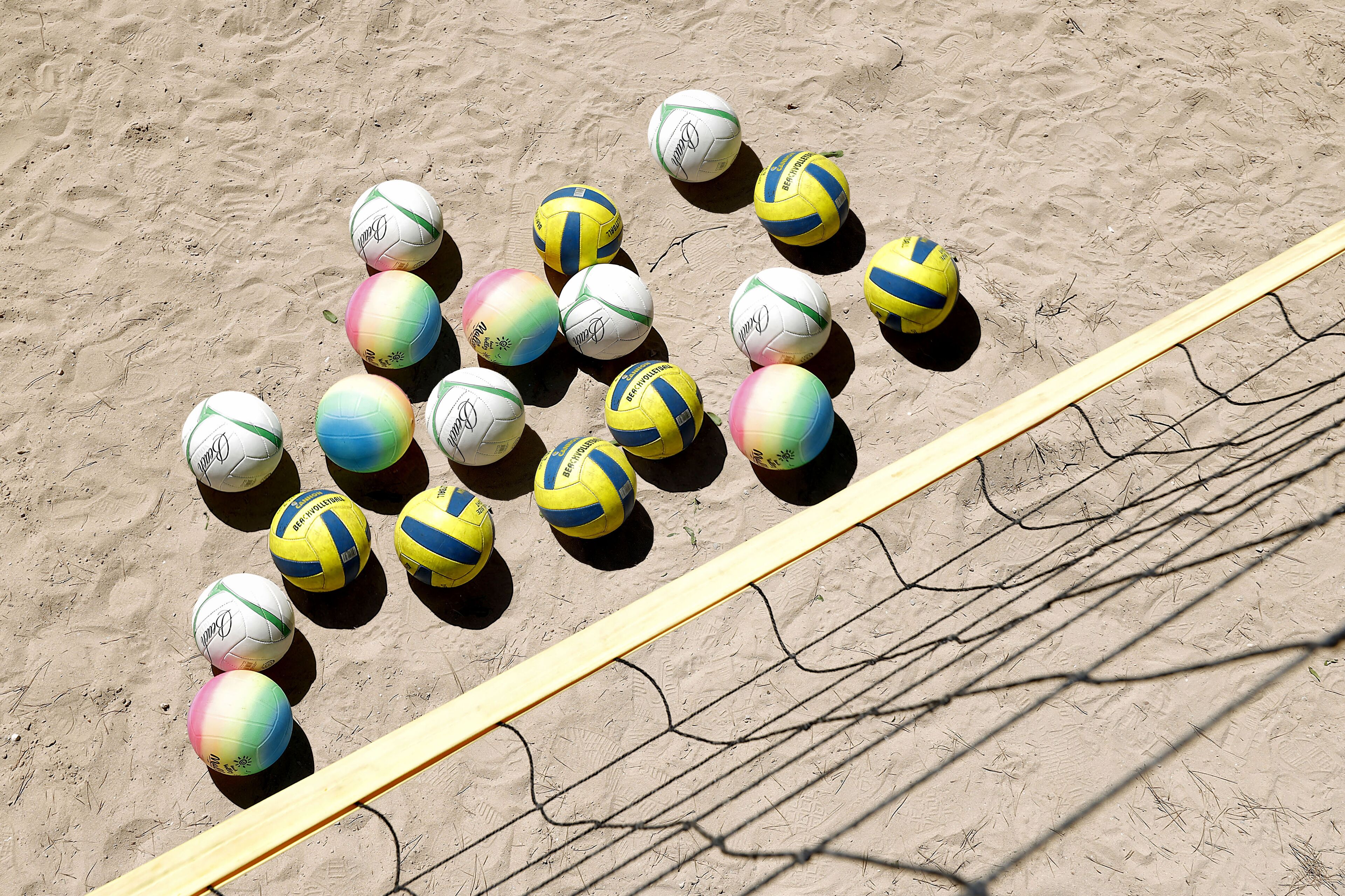 Una red de voleibol de playa con varios voleibolillos de colores dispuestos sobre la arena.