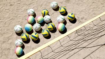 Una red de voleibol de playa con varios voleibolillos de colores dispuestos sobre la arena.