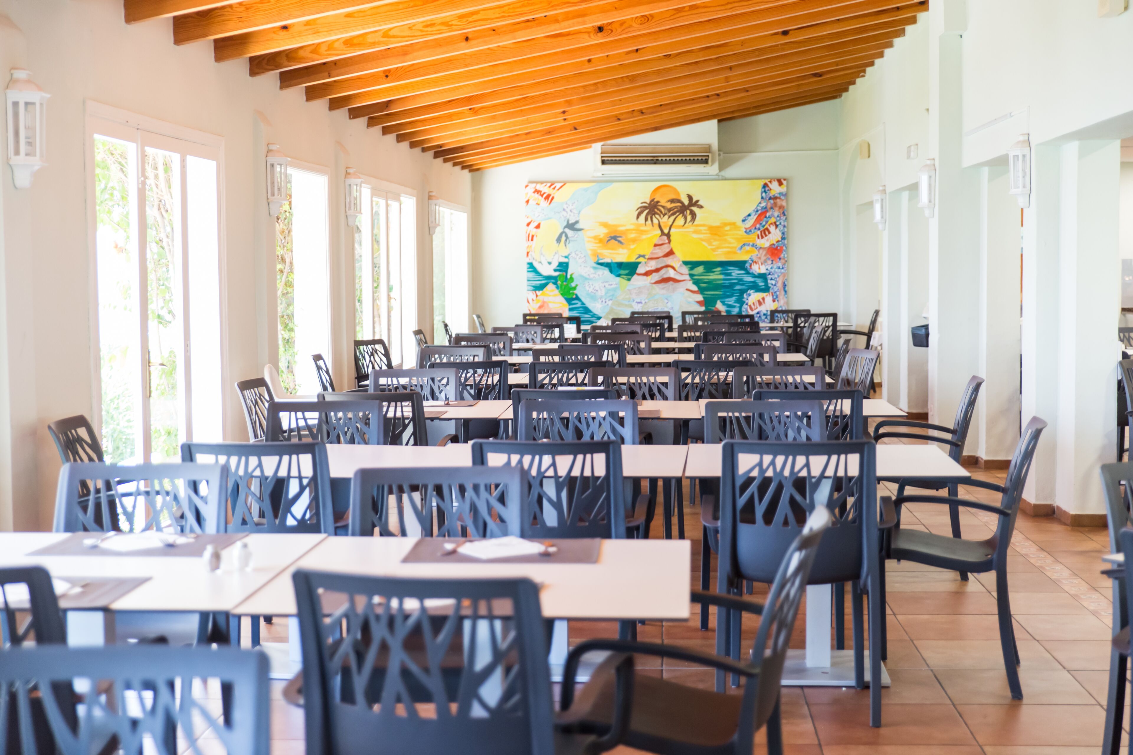 Un vaste espace dédié à la salle à manger, avec de nombreuses tables et chaises, de grandes fenêtres et une fresque murale.