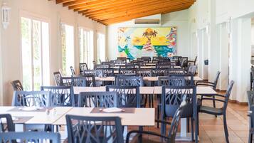 Un vaste espace dédié à la salle à manger, avec de nombreuses tables et chaises, de grandes fenêtres et une fresque murale.