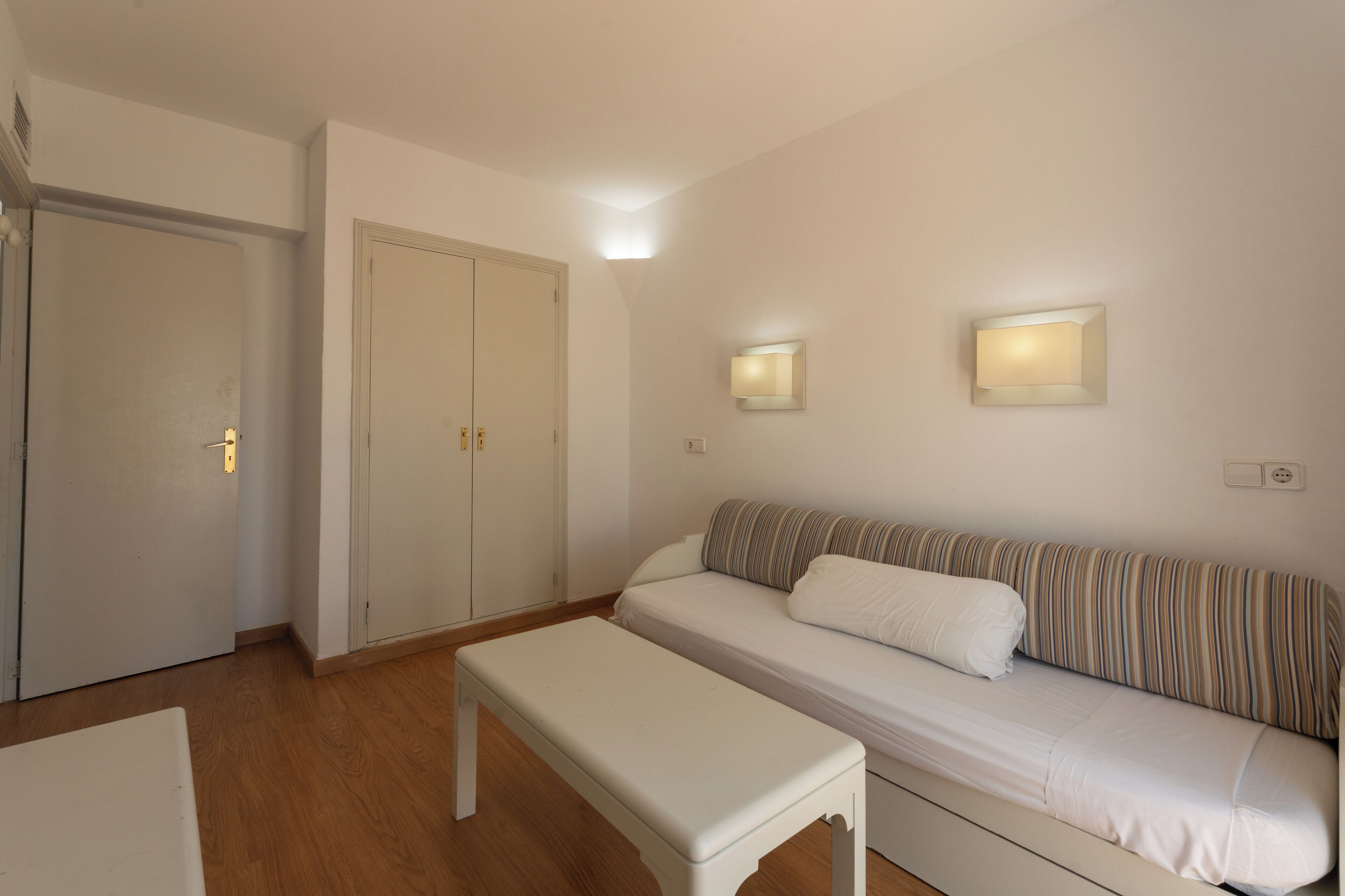 A room with a sofa, an ottoman, and a wardrobe.