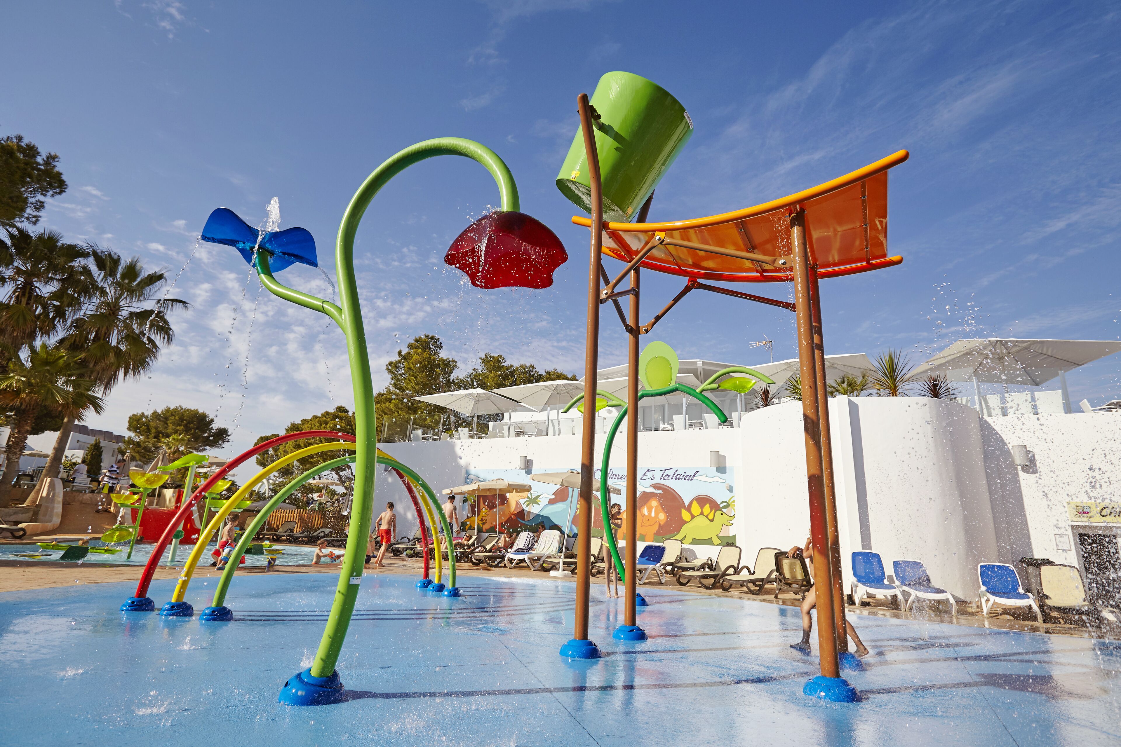 A water play area with colorful structures and a pool in the background.