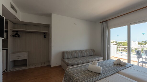 A hotel room with a bed, a seating area, a wardrobe, and a view of the outside.