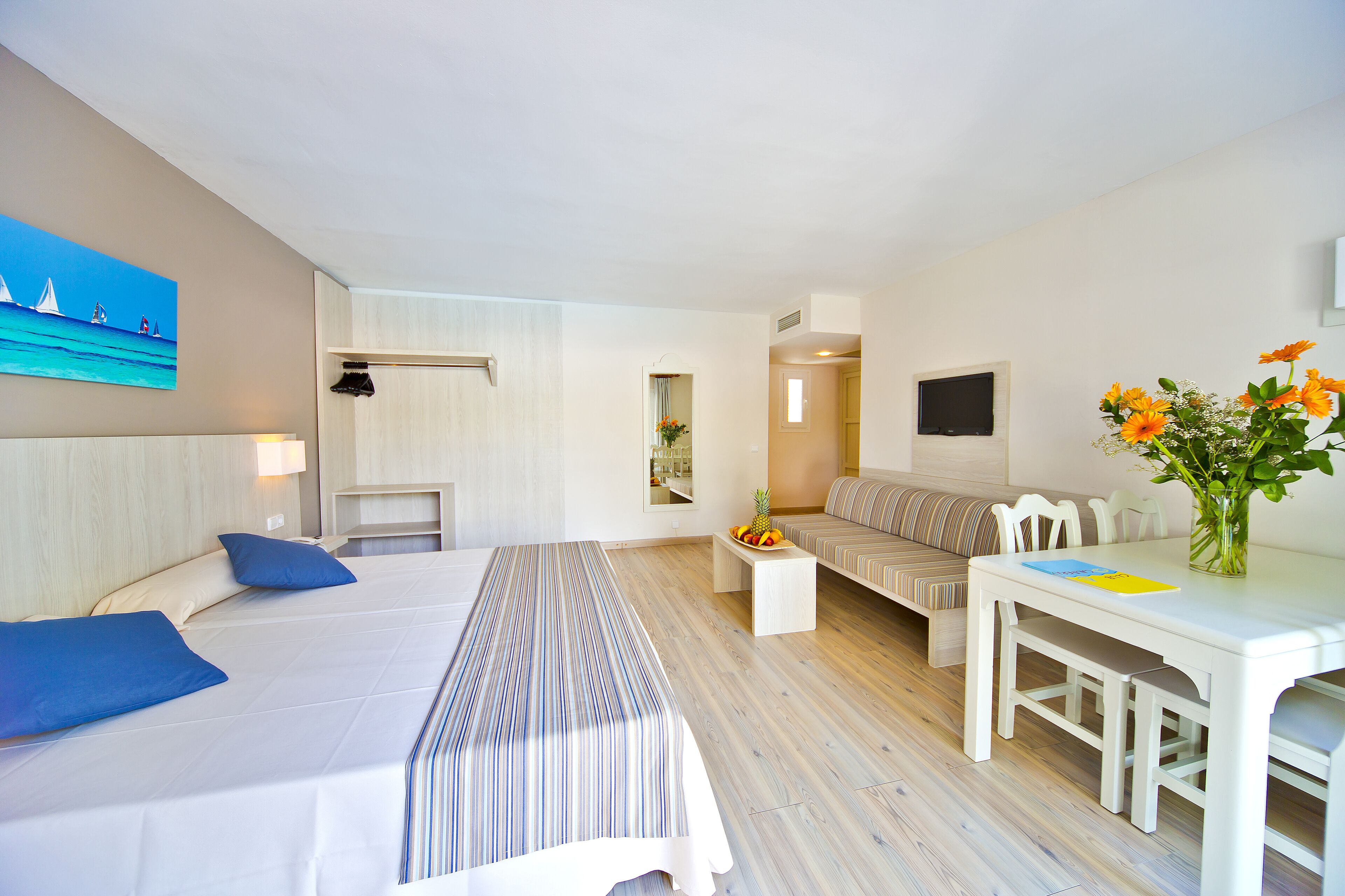 A hotel room with a large bed, a sofa, a dining table, and a TV.