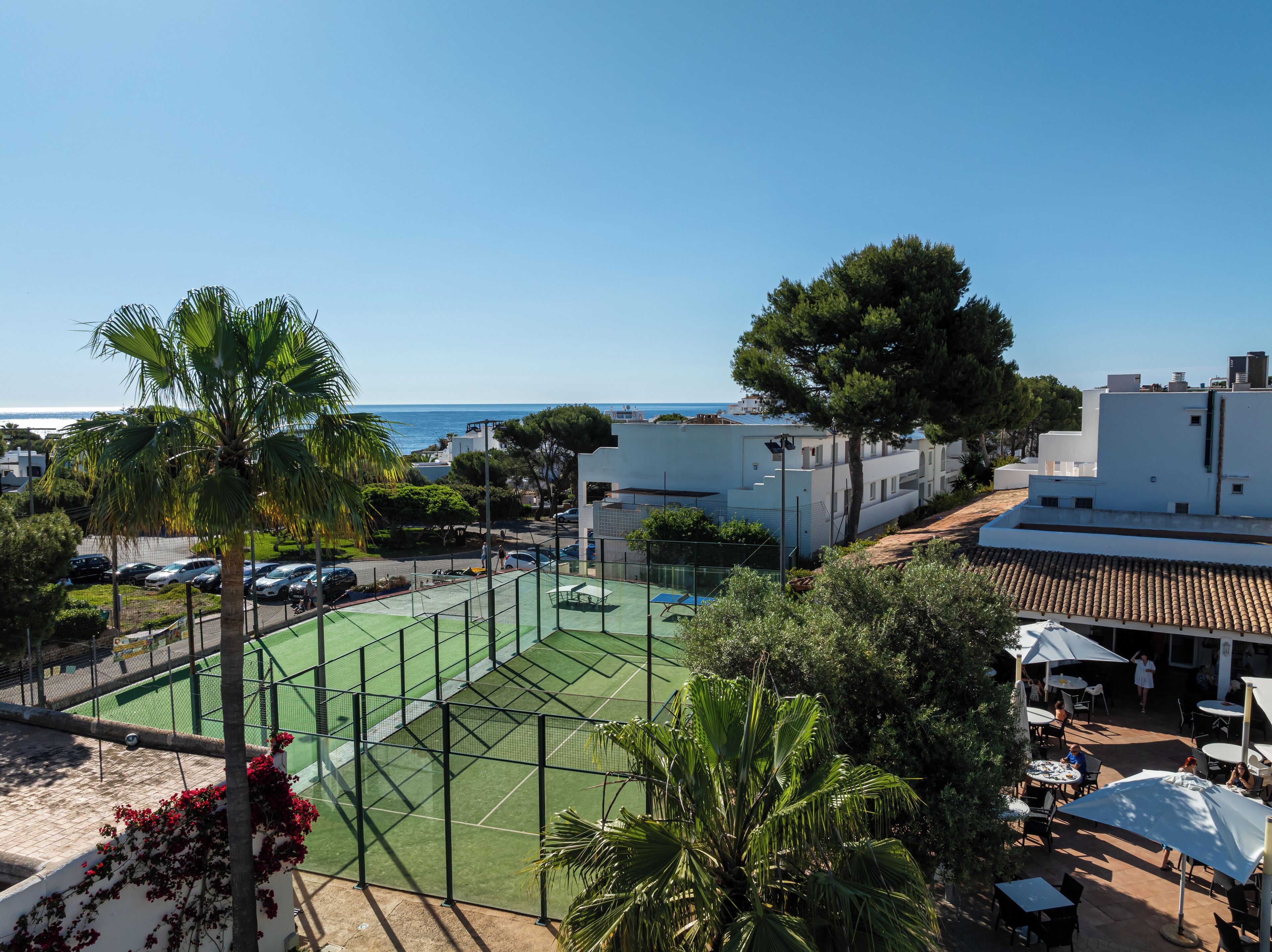 Ein Tennisplatz mit Netz, umgeben von Grünflächen und Blick auf das Meer.