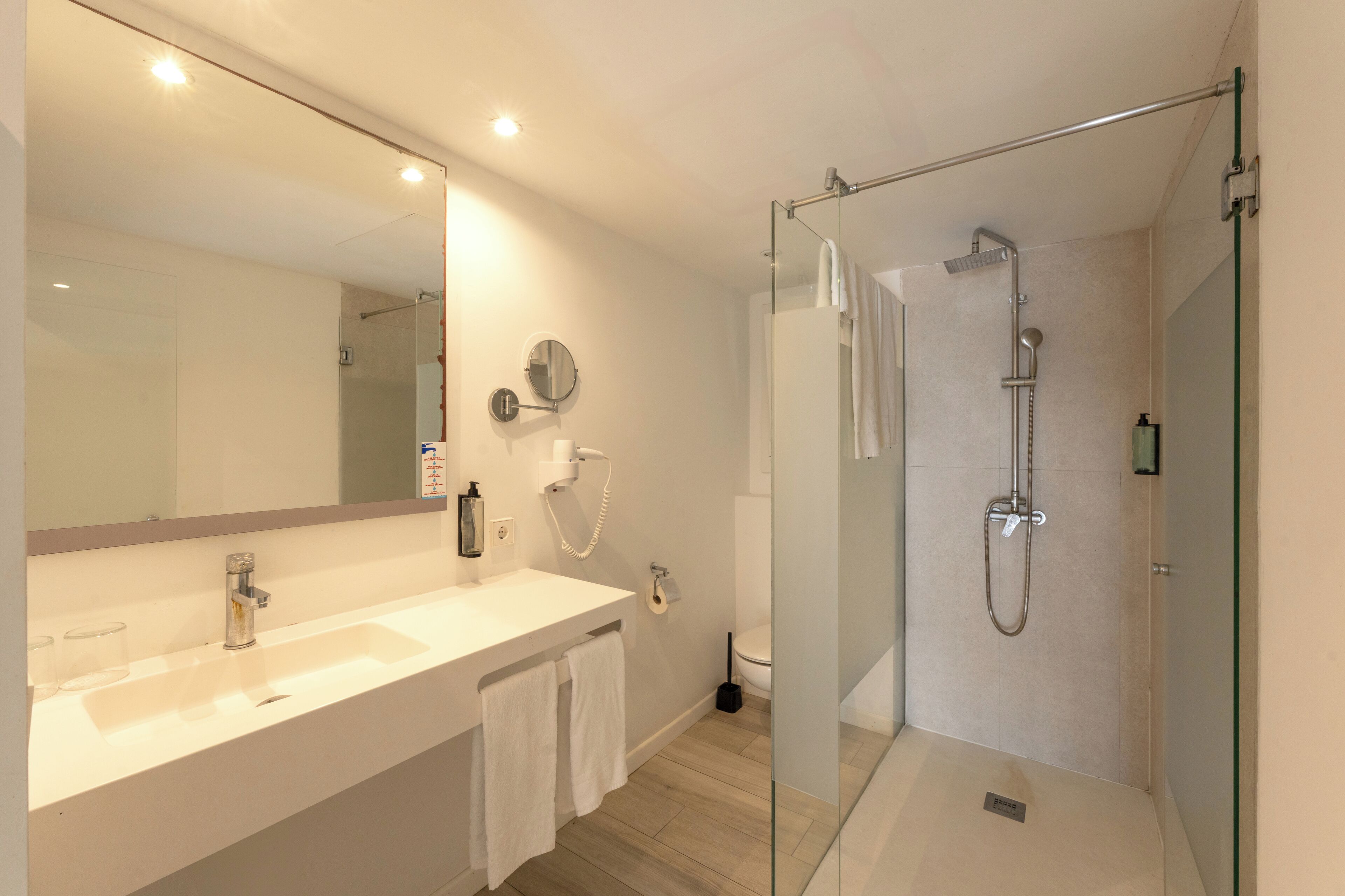 A modern bathroom with a glass-enclosed shower, a large mirror, and a white vanity with a sink and towel rack.