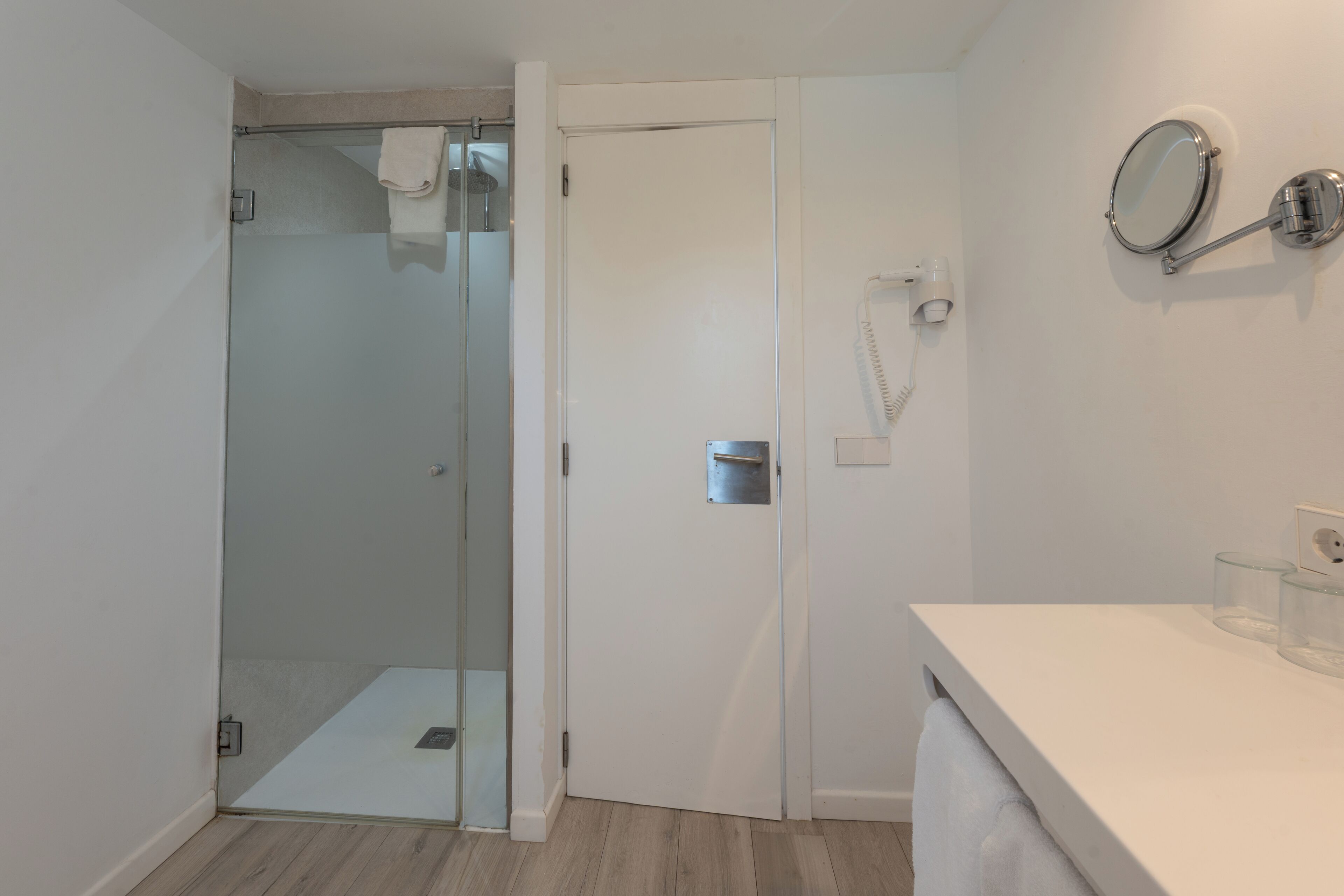 A bathroom with a glass shower enclosure, a white sink with a mirror, and a towel hanging on the door.