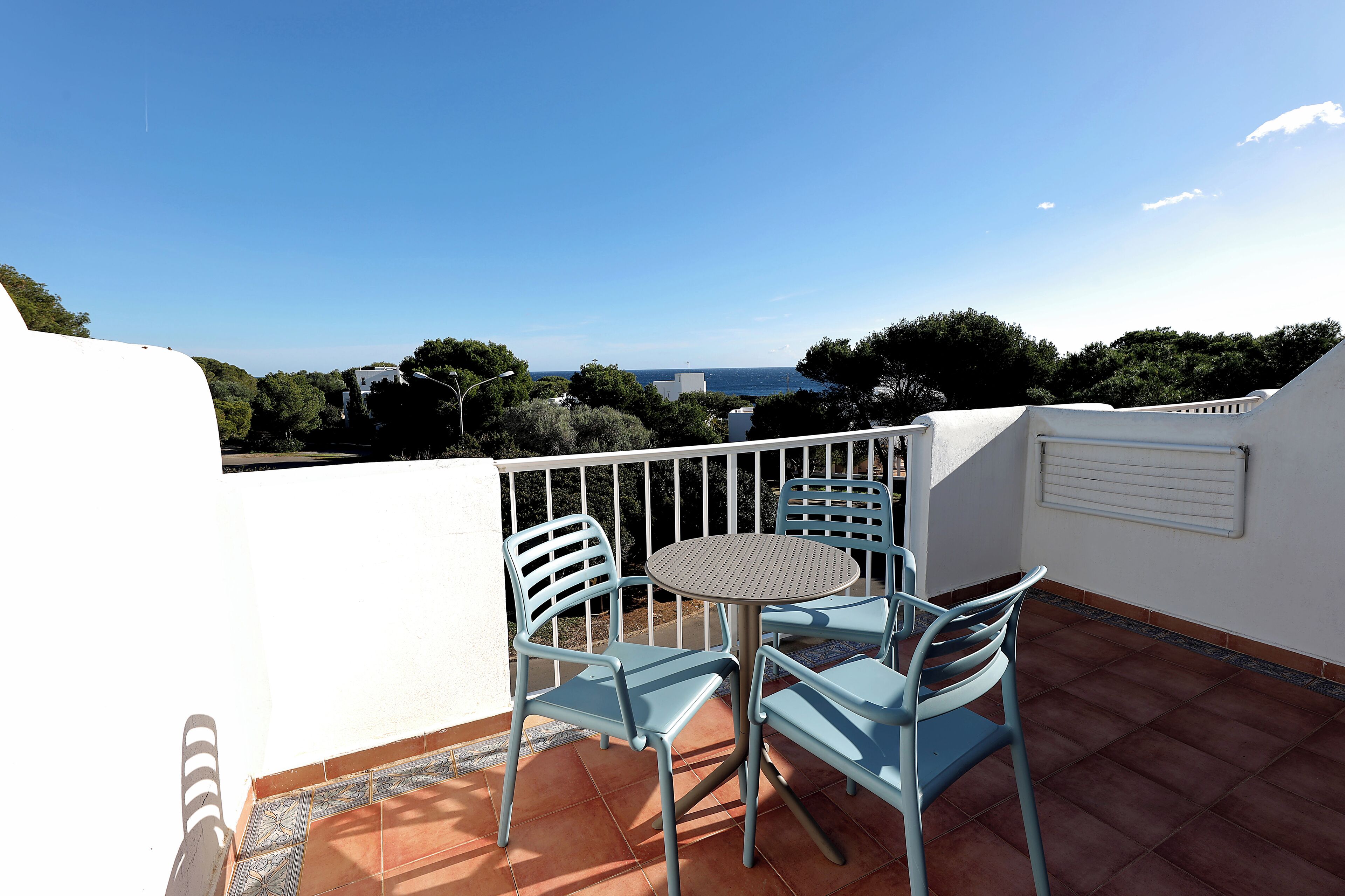 A balcony with a table and chairs, overlooking a scenic view of the sea and trees.