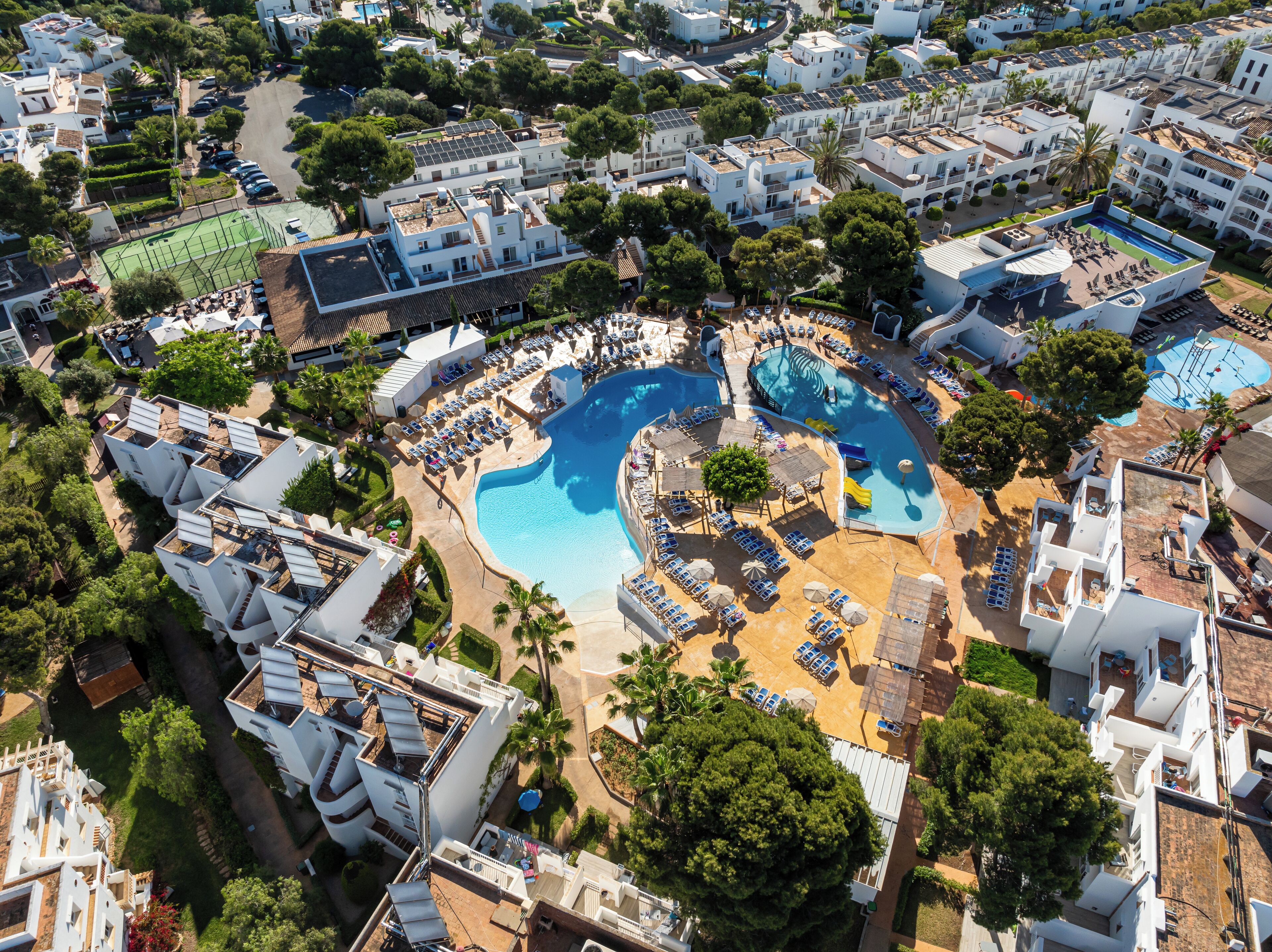 Luchtbeeld van een resort met meerdere zwembaden, ligbedden en een verzorgd landschap.
