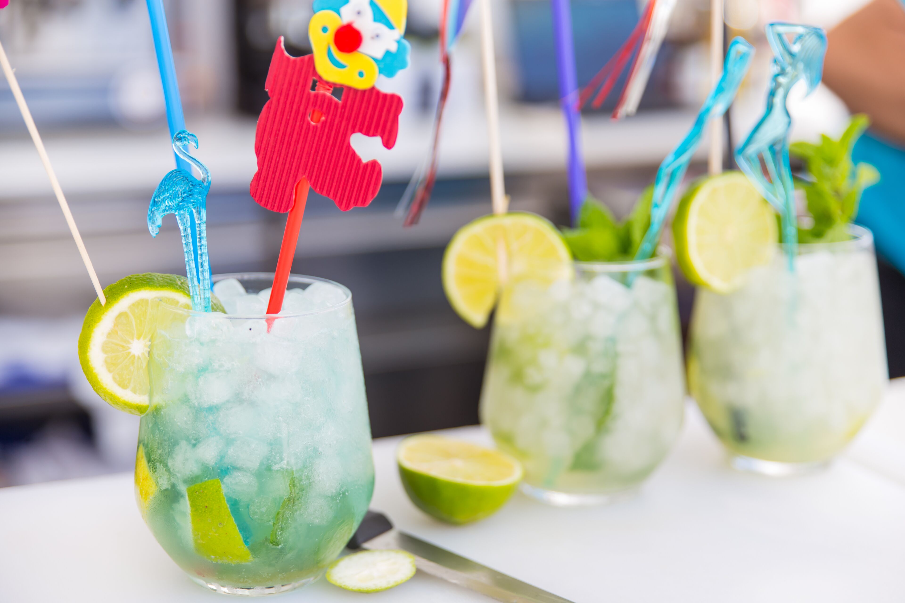 A close-up of three drinks with colorful straws and lime wedges.