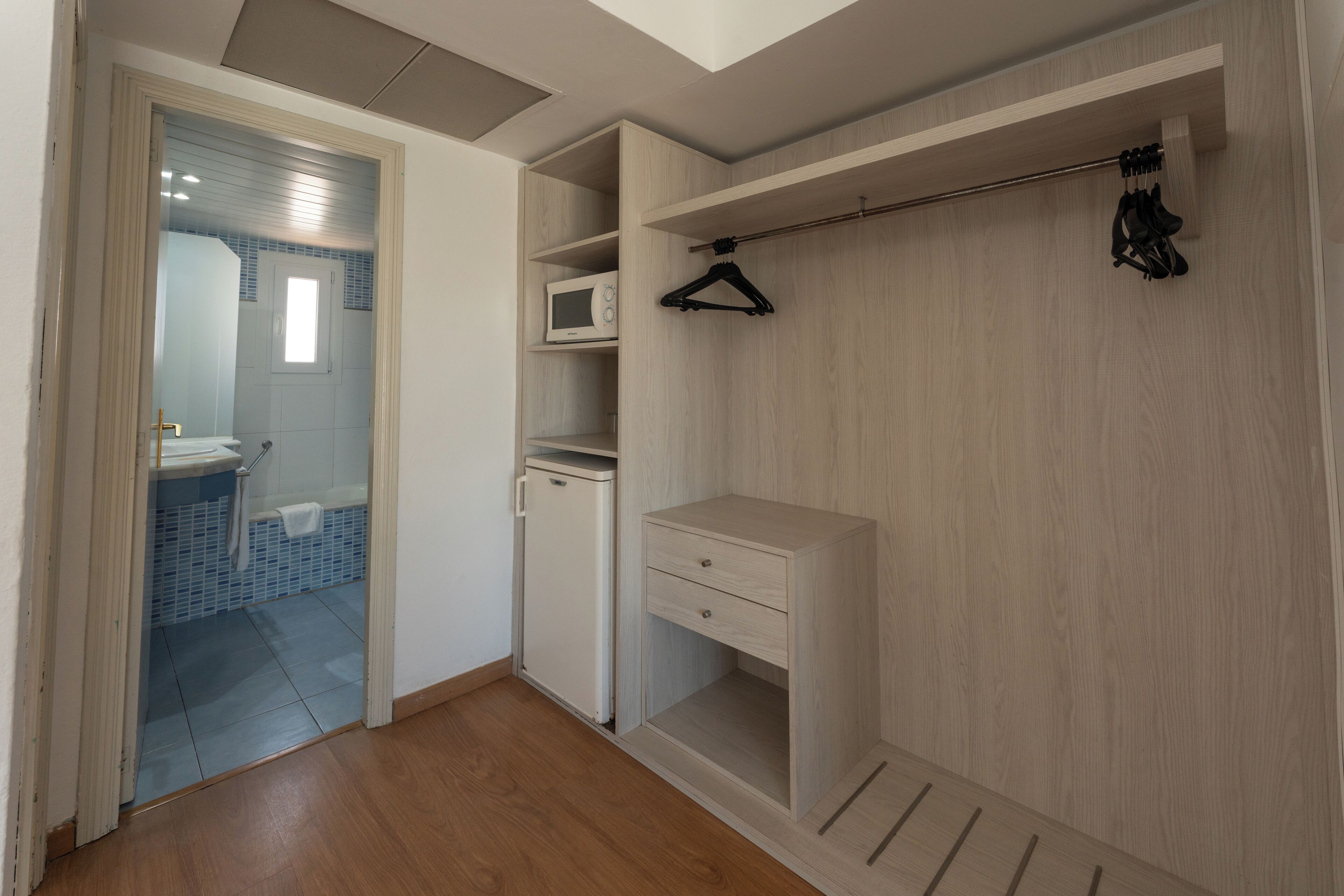 Un vestidor con microondas, perchero y un mueble pequeño.