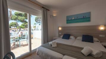 A hotel room with a bed, a painting of sailboats, and a view of an outdoor pool area.