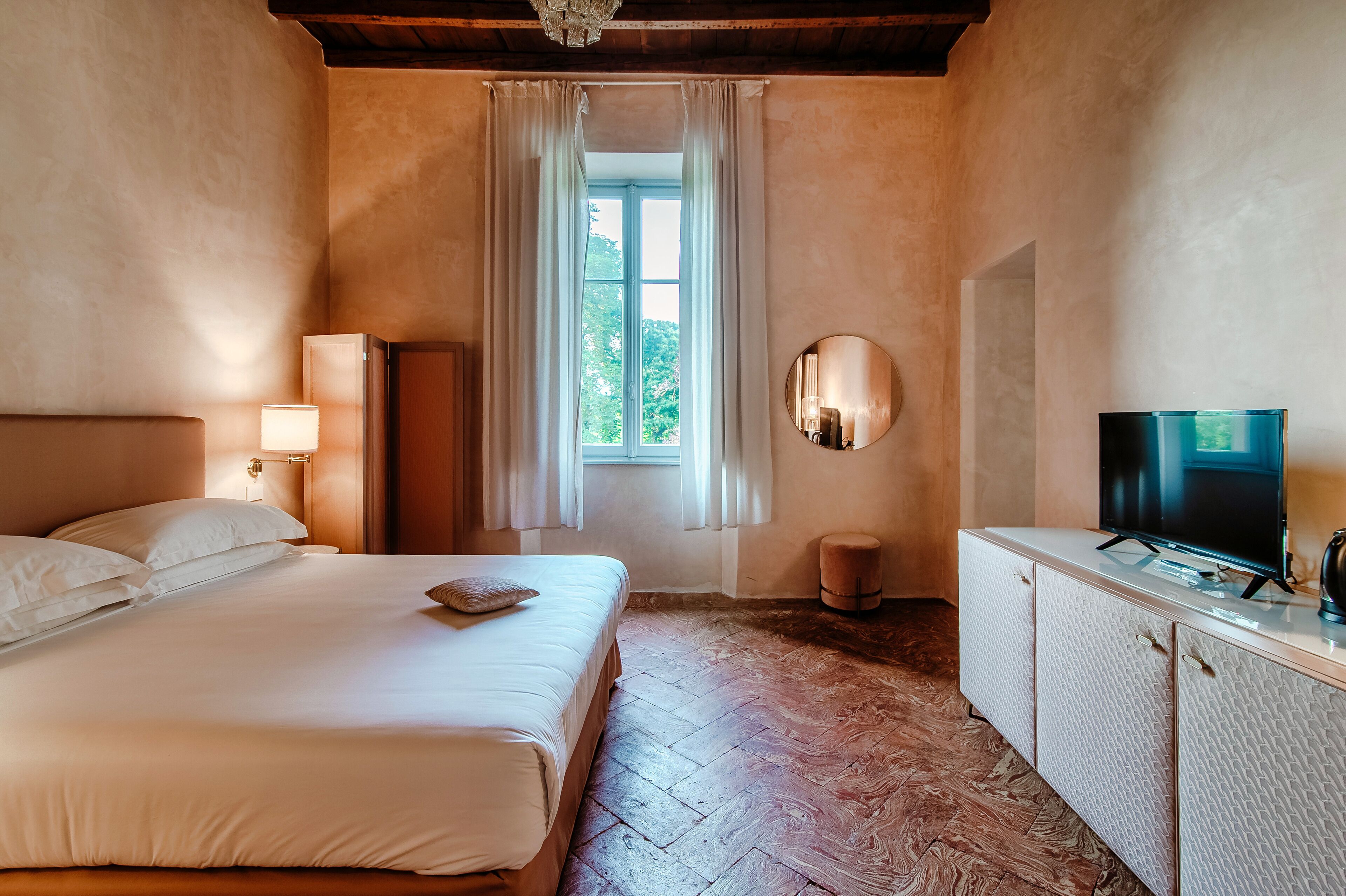 Ein Schlafzimmer mit Bett, Fernseher, Spiegel und einem Fenster mit Vorhängen.