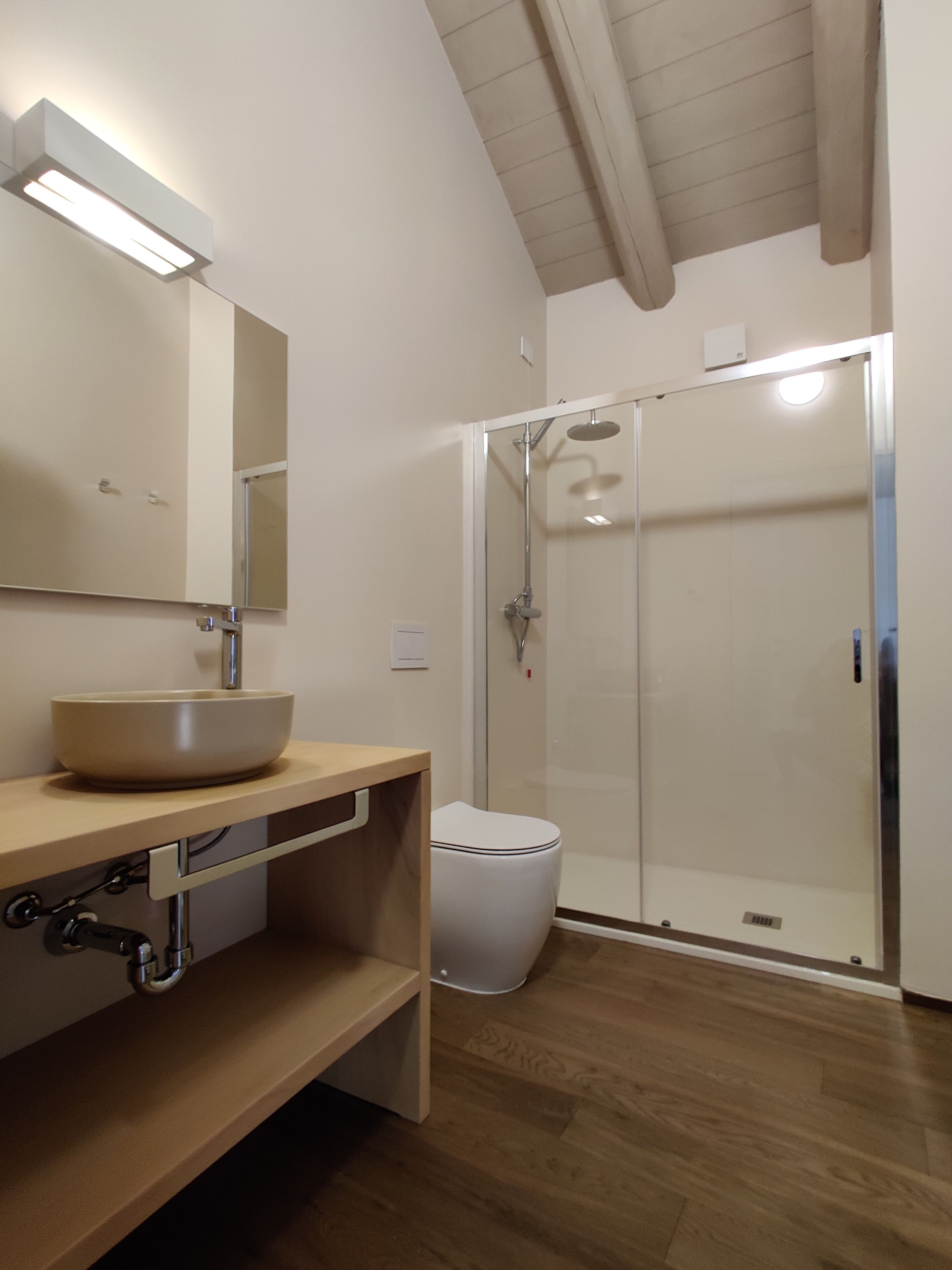 Ein modernes Badezimmer mit Waschtisch aus Holz, einem großen Spiegel, einer weißen Spüle, einer Toilette und einer Duschkabine.