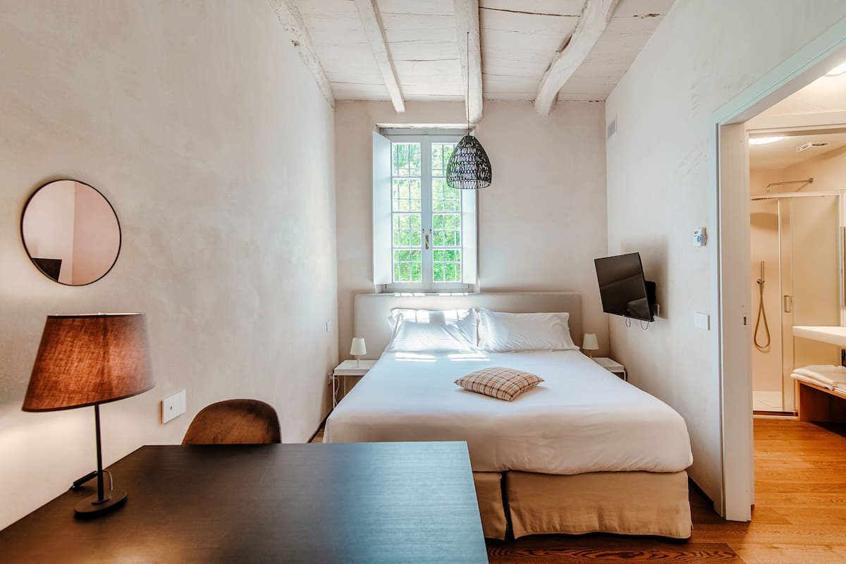 A bedroom with a bed, bedside table, lamp, and a TV.