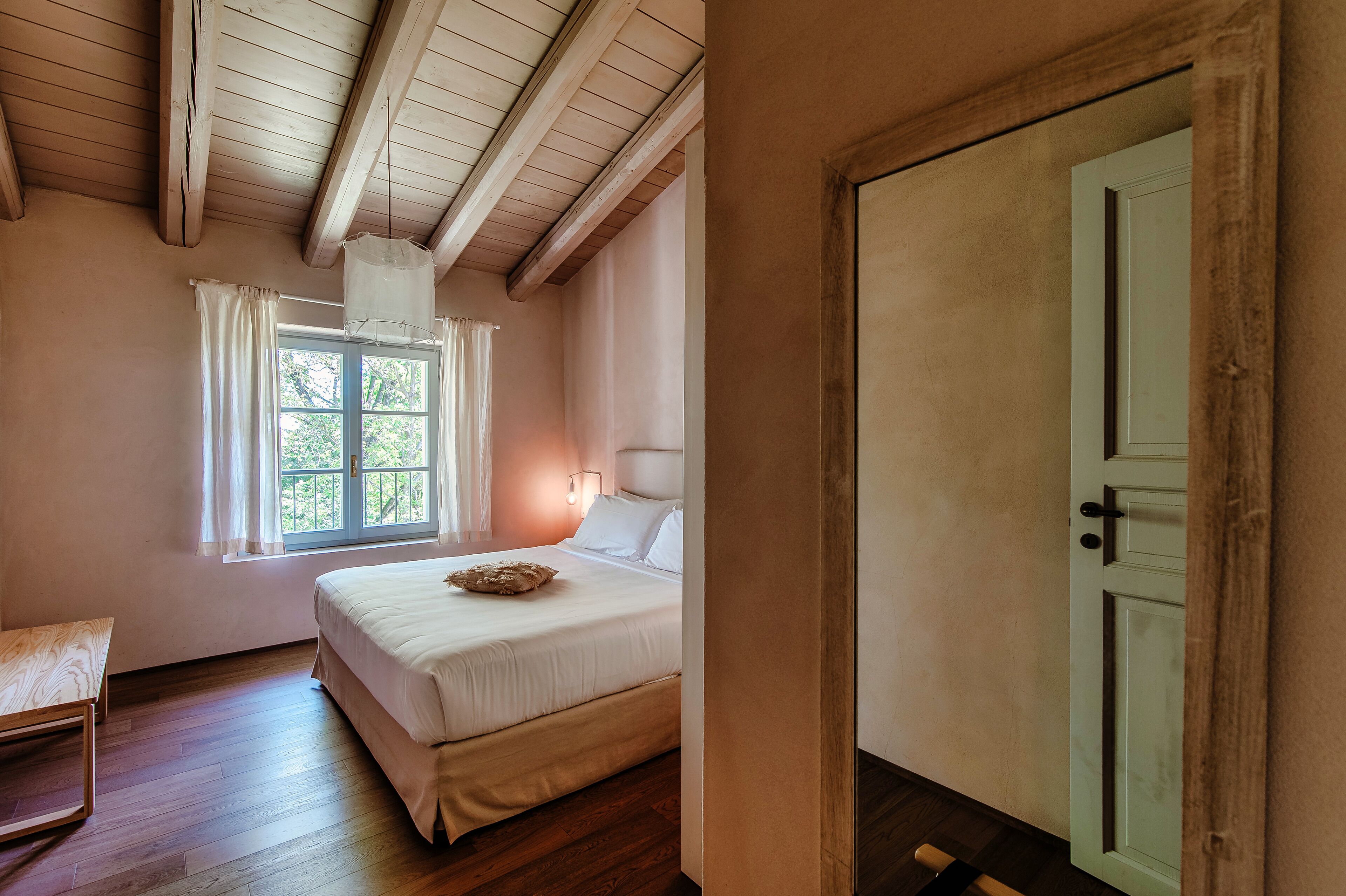 Un dormitorio con cama, una banca, una ventana con cortinas y una puerta.