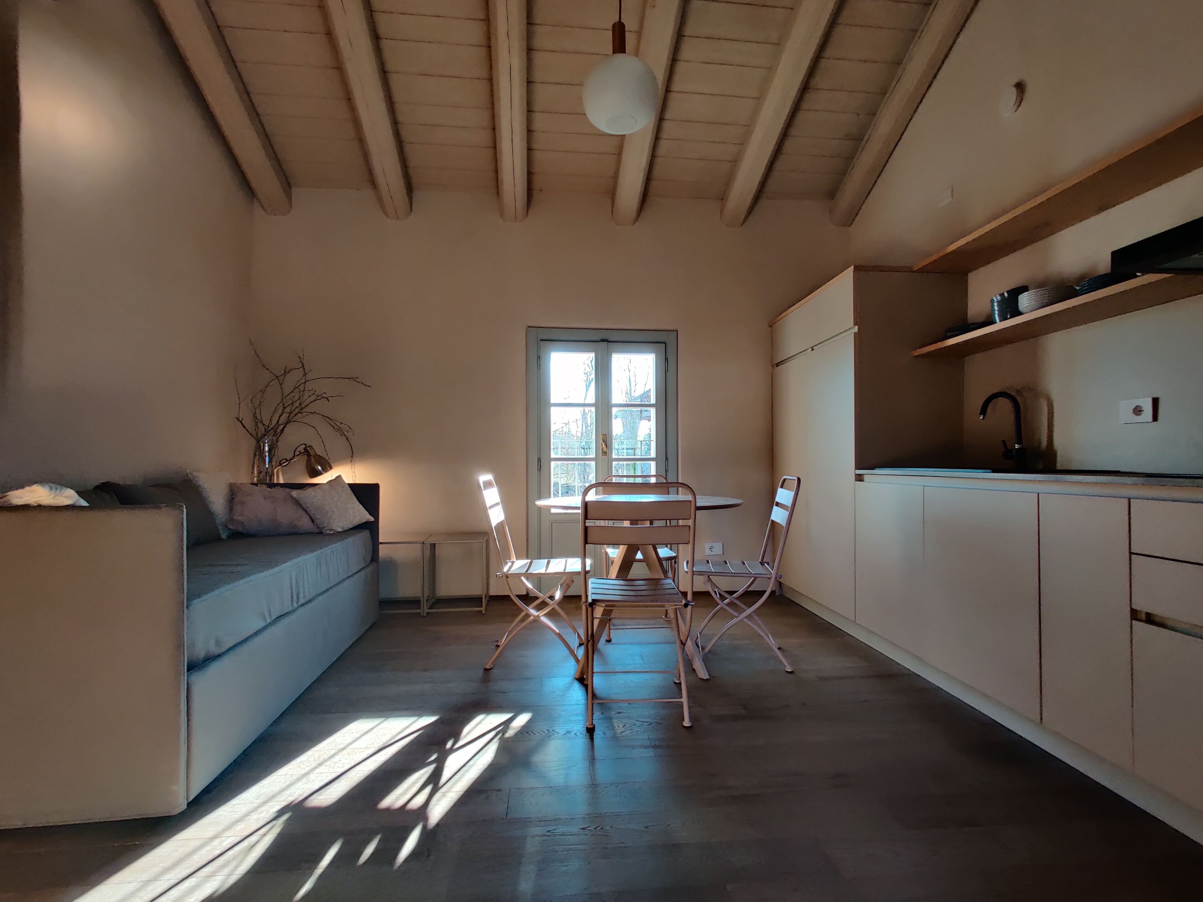 Eine moderne Küche mit Essbereich, Holzbalken an der Decke und einem großen Fenster, das für natürliches Licht sorgt.