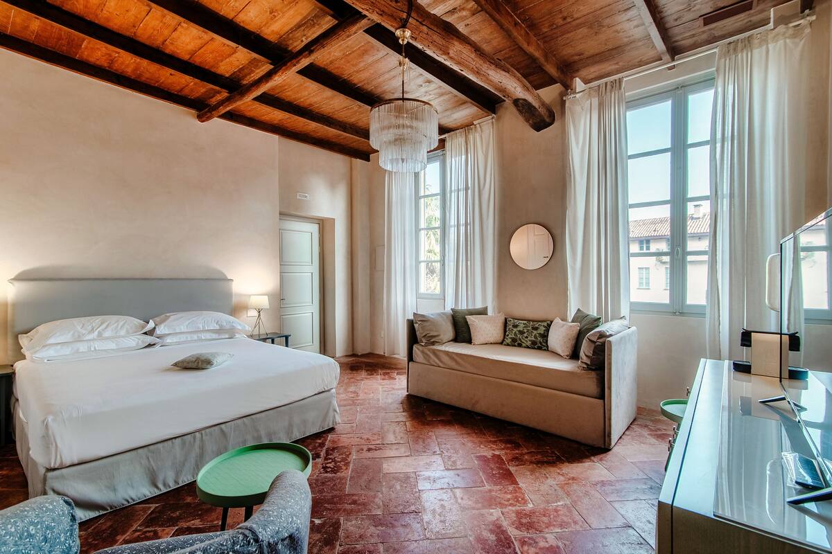 A bedroom with a bed, a sofa, a desk, and a large window with curtains.