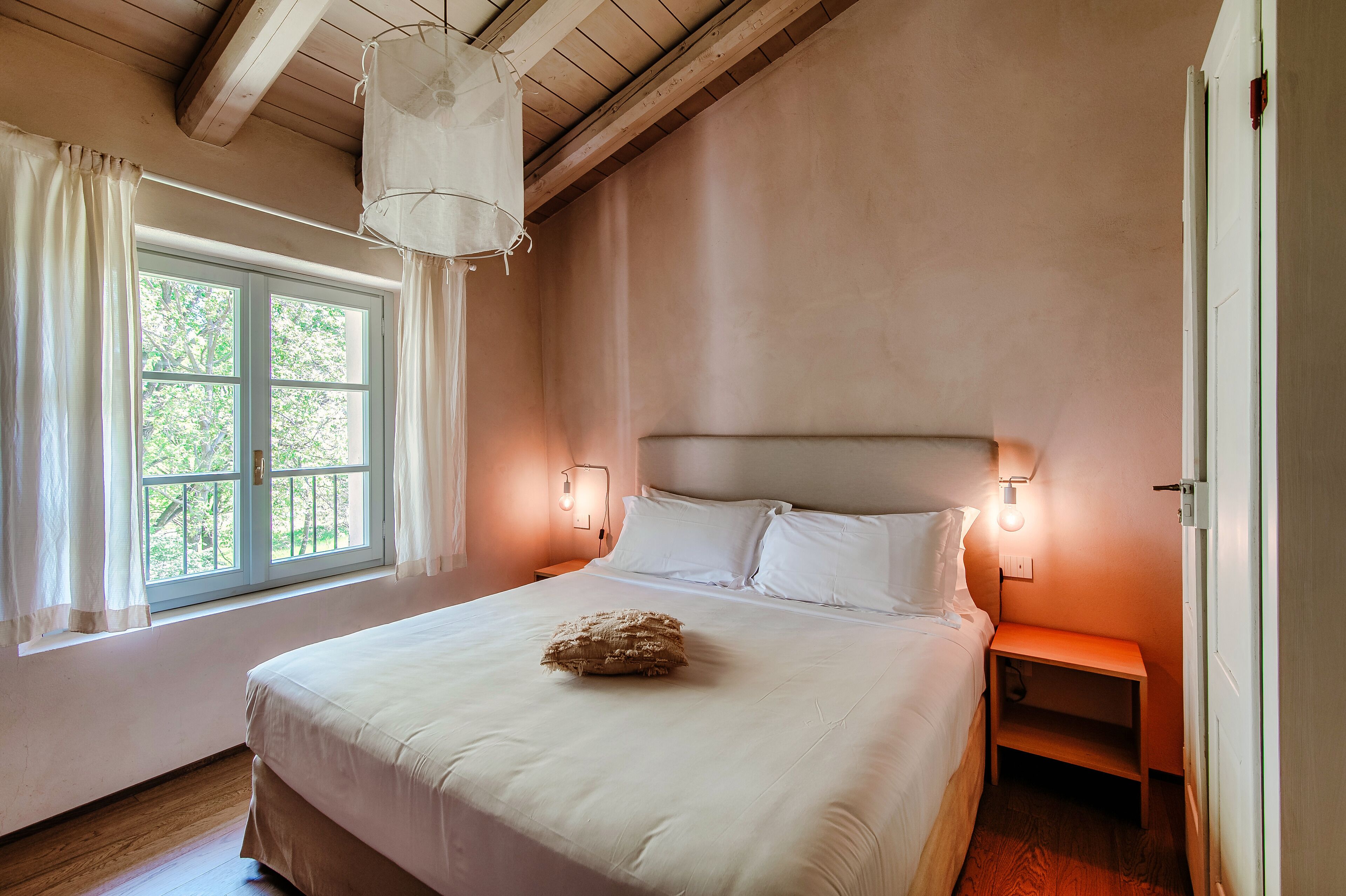 Un dormitorio con una cama grande, dos lámparas de noche, una mesita de noche y una ventana con cortinas.