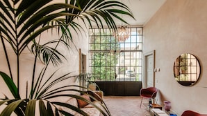 Una habitación amplia con una planta grande en maceta, una silla roja y un espejo redondo en la pared.