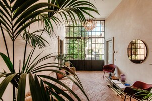 Una habitación amplia con una planta grande en maceta, una silla roja y un espejo redondo en la pared.
