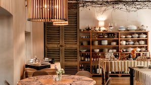 Un comedor con una mesa de madera dispuesta para dos personas, una estantería de madera con varios platos y botellas, y una lámpara colgante.