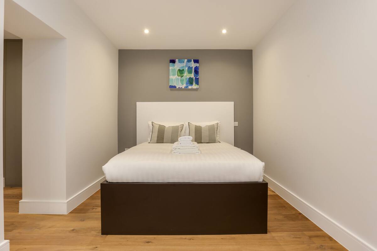 A bedroom with a bed, a headboard, a wall-mounted artwork, and a wooden floor.