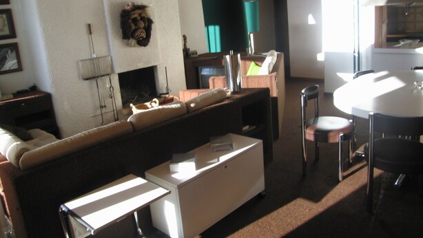 Una sala de estar con sofá, una mesita, chimenea y un comedor con mesa y sillas.