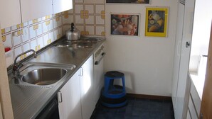 Una cocina compacta con armarios blancos, un lavamanos de acero inoxidable y un taburete azul.