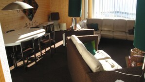 Una sala de estar con sofá, mesa de comedor con sillas, lámpara y ventana con persianas.