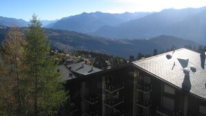 Un albergue de montaña con varios balcones, vistas de las montañas circundantes y un cielo despejado.