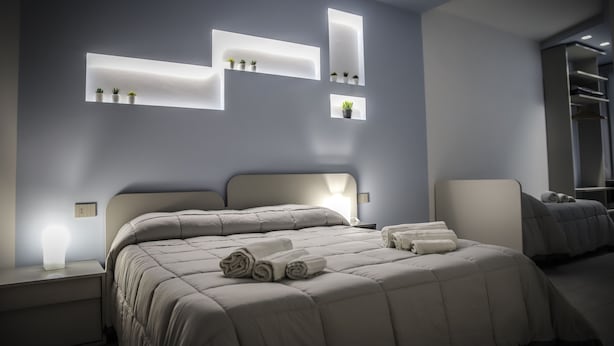 A modern bedroom with a large bed, bedside tables, and built-in shelves with plants. - Urban Relax (Favara)