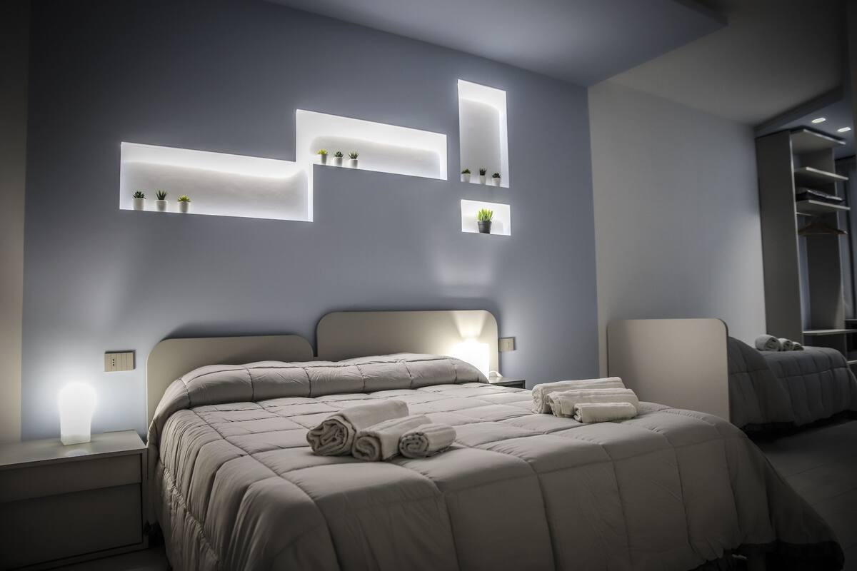 A modern bedroom with a large bed, bedside tables, and built-in shelves with plants.