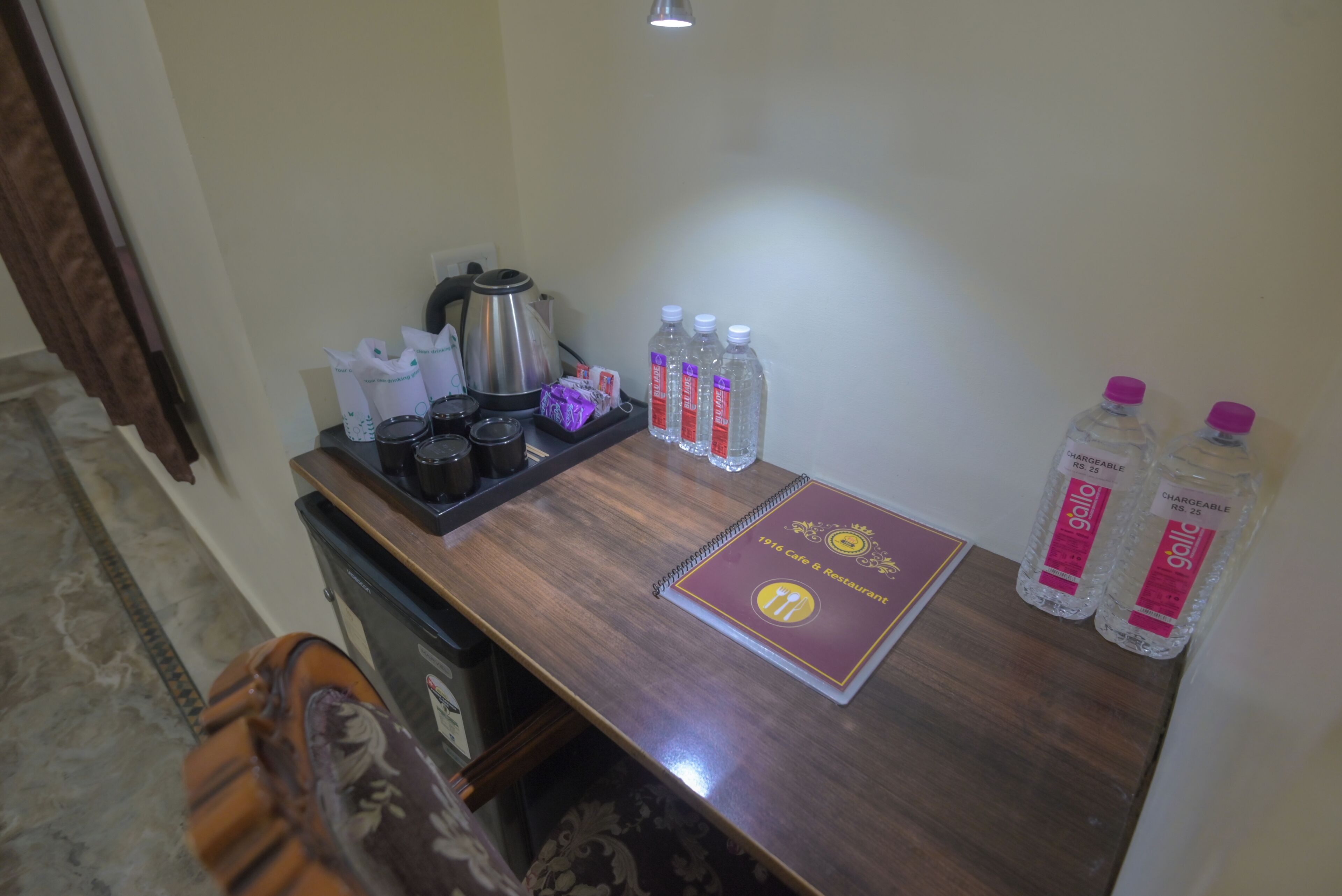 Un bureau en bois avec un carnet, une bouilloire, des tasses et des bouteilles d’eau.