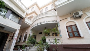 Un patio con una escalera central, plantas en macetas y fachada de edificio con ventanas de arco y barandillas decorativas.