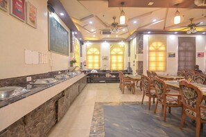 A hotel dining area with a buffet setup, seating arrangements, and a chalkboard with writing. - Shree Ganesha Residency (Varanasi)