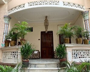 Entrada de un edificio con puerta de madera, plantas en macetas y barandilla decorativa blanca.