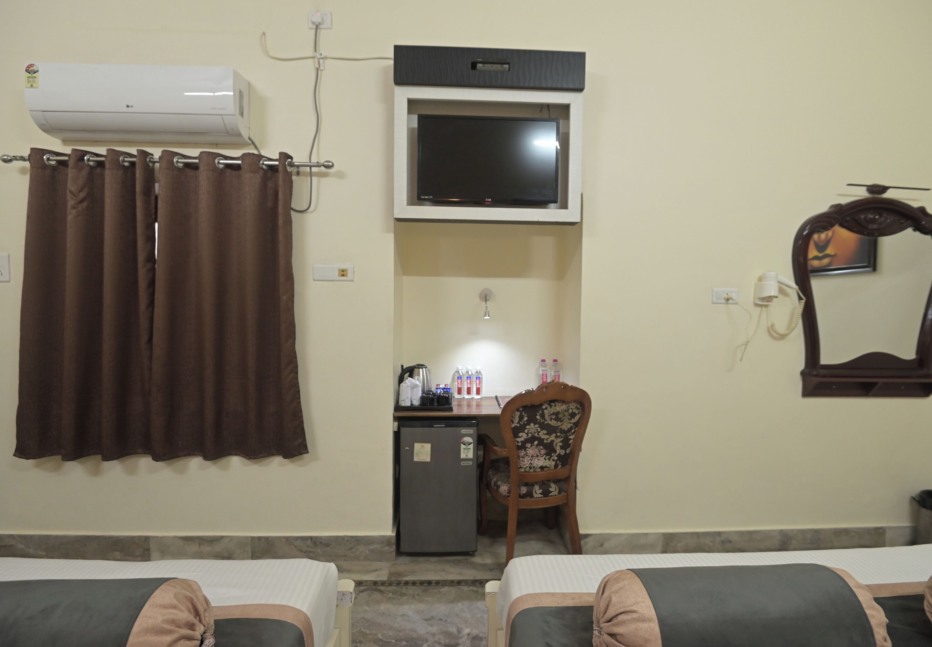A hotel room with a bed, a desk with a television, a mirror, and a small refrigerator.