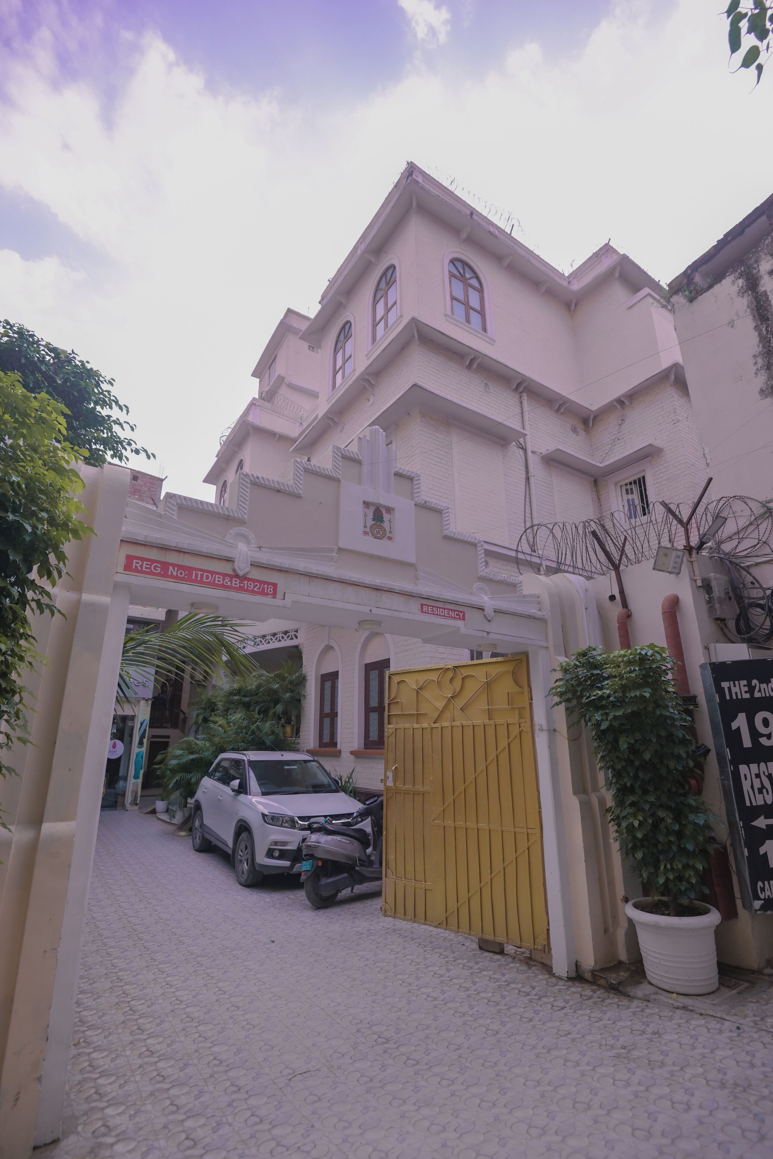 A building with a gated entrance, a sign indicating a residency, and a parked car.