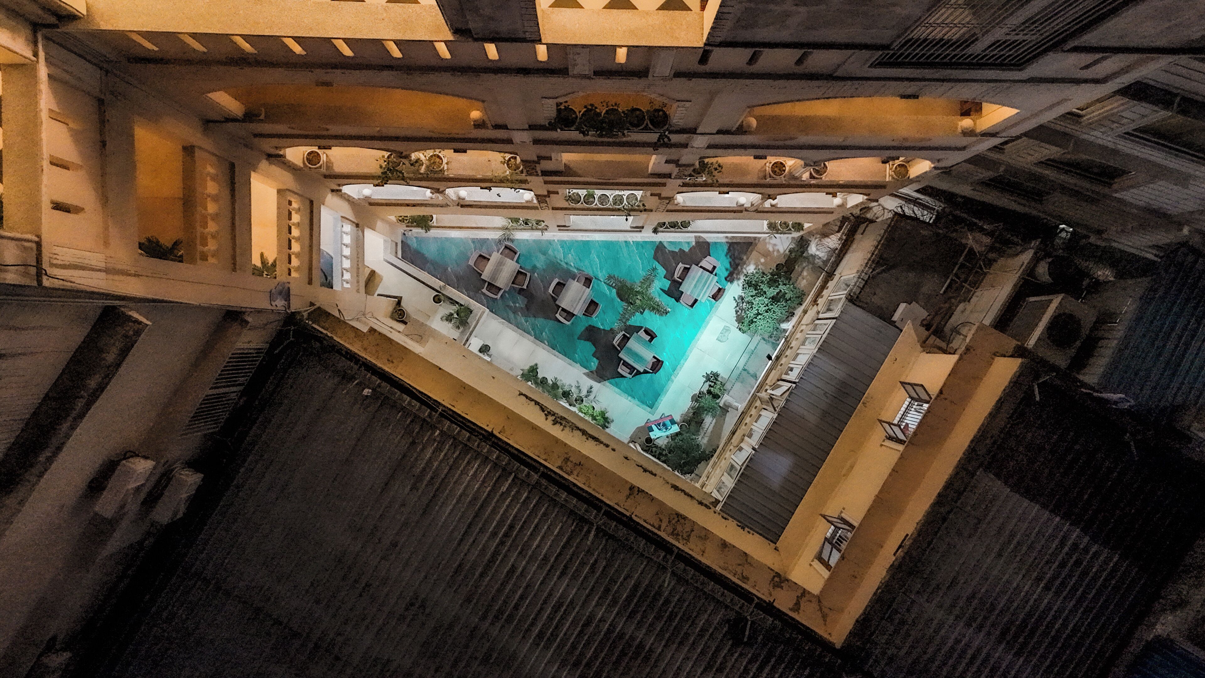 Vista aérea de un área de piscina en la azotea con varios espacios de descanso y una fuente central.