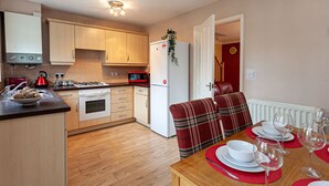 A compact kitchen with wooden cabinets, a white refrigerator, and a dining area with a table set for four. - Irlam's Home from Home (Manchester)