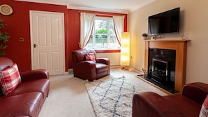 A living room with red walls, a fireplace, a television, and two leather sofas. - Irlam's Home from Home (Manchester)