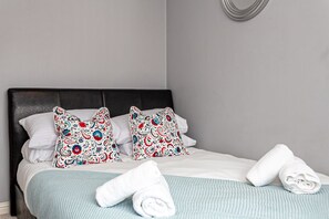 A neatly made bed with a blue blanket, two decorative pillows, and rolled white towels. - Irlam's Home from Home (Manchester)