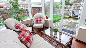 A conservatory with wicker furniture, a glass table, and a view of a garden. - Irlam's Home from Home (Manchester)