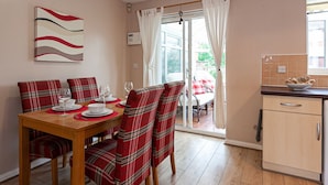 A dining area with a wooden table and plaid chairs, a kitchen with a tiled backsplash, and a sliding glass door leading to an outdoor area. - Irlam's Home from Home (Manchester)