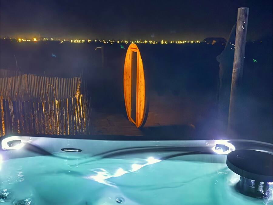 Hidromassatge amb estructura de fusta al fons, un pal de fusta, i vista a una riba il·luminada.