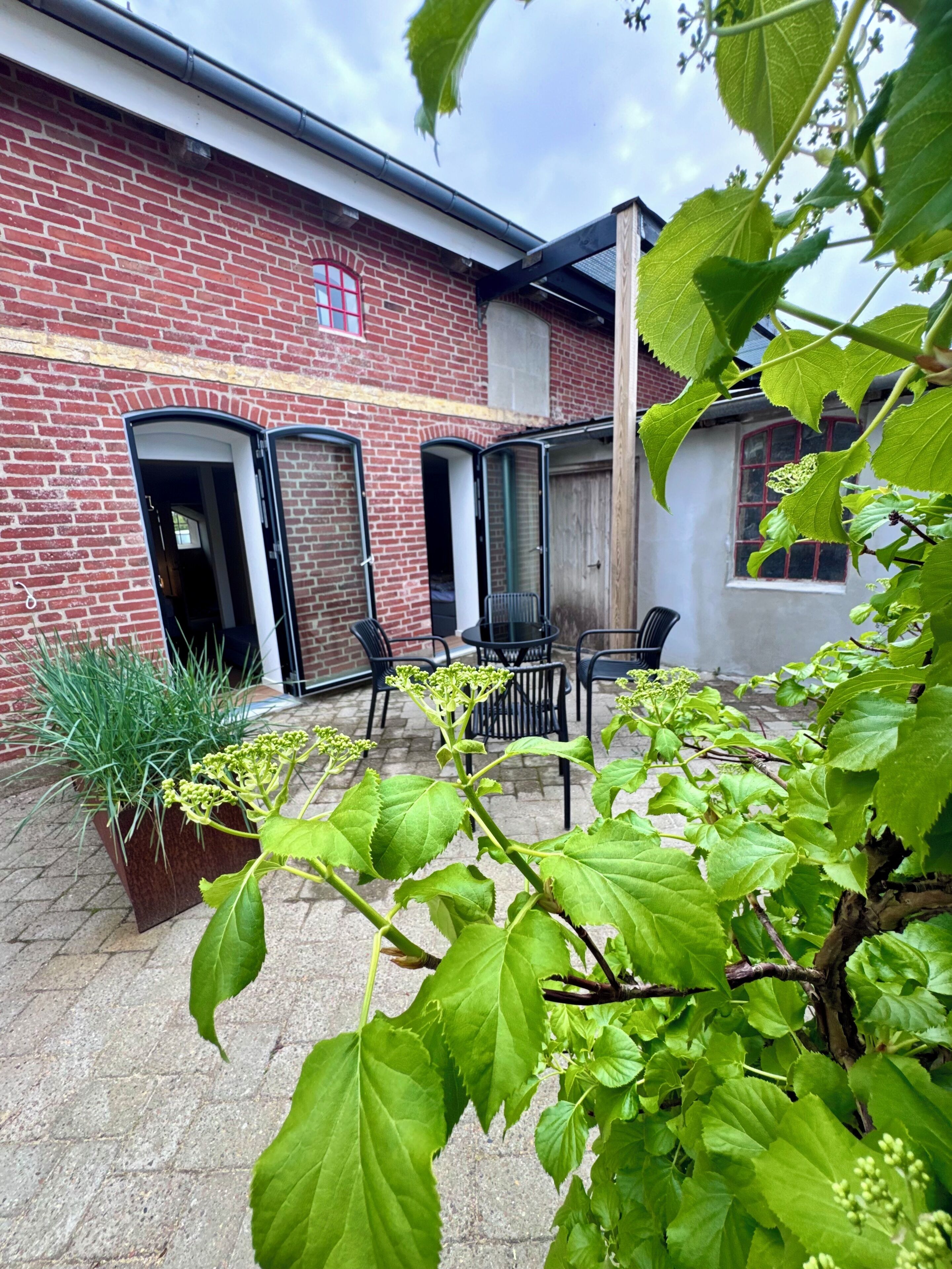 Ein Backsteingebäude mit Innenhof, Außenbestuhlung und einem Blumentopf.